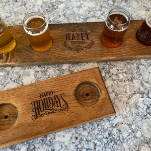 May include: Two wooden serving trays with a "Happy Holidays" inscription. The larger tray has three slots for holding glasses, while the smaller tray has two slots. Both trays are made of natural wood with a rustic finish.