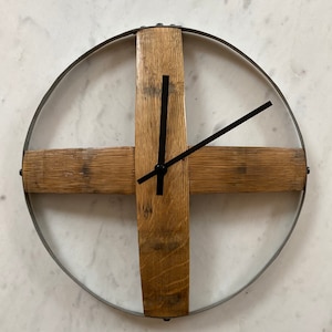 Könnte beinhalten: Eine runde Wanduhr aus recyceltem Holz und Metall. Das Zifferblatt der Uhr ist weiß mit schwarzen Zeigern. Die Uhr ist an einer weißen Wand montiert.