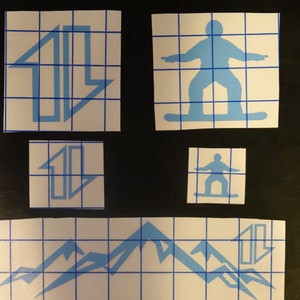 May include: Four blue vinyl stickers on a white gridded background. The stickers feature a mountain range, a snowboarder, and two different designs of an arrow pointing upwards.