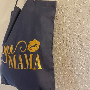 May include: A navy blue tote bag with gold lettering that says "Yee to Mama" with a gold glitter lip print.