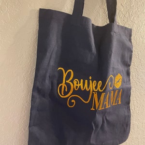 May include: A navy blue tote bag with gold glitter lettering that says "Boujee Mama" with a gold glitter lip print.