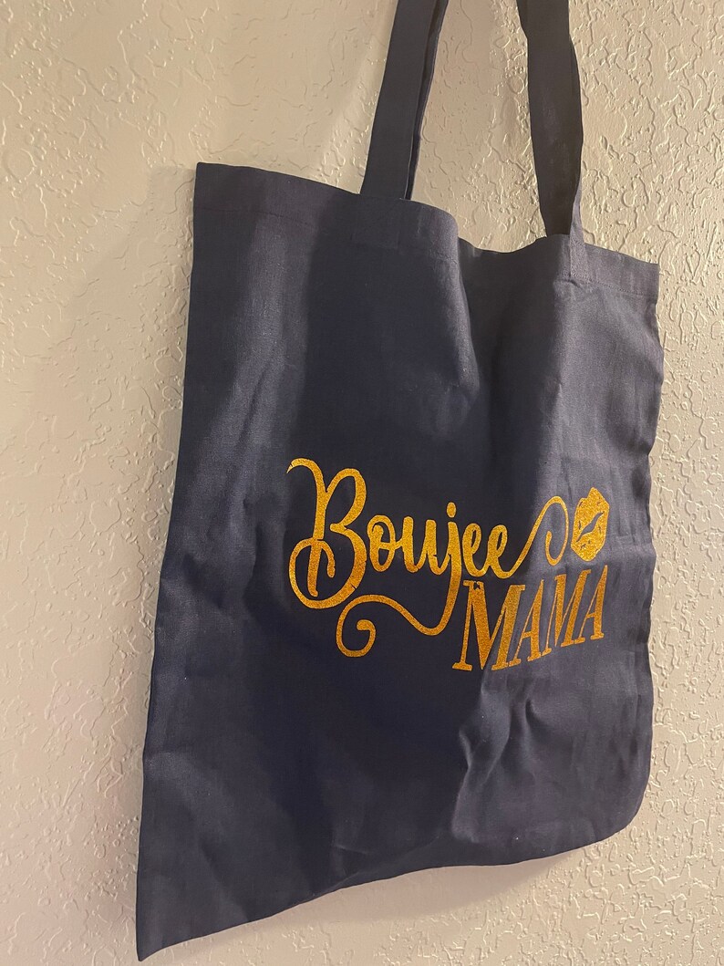 May include: A navy blue tote bag with gold glitter lettering that says "Boujee Mama" with a gold glitter lip print.