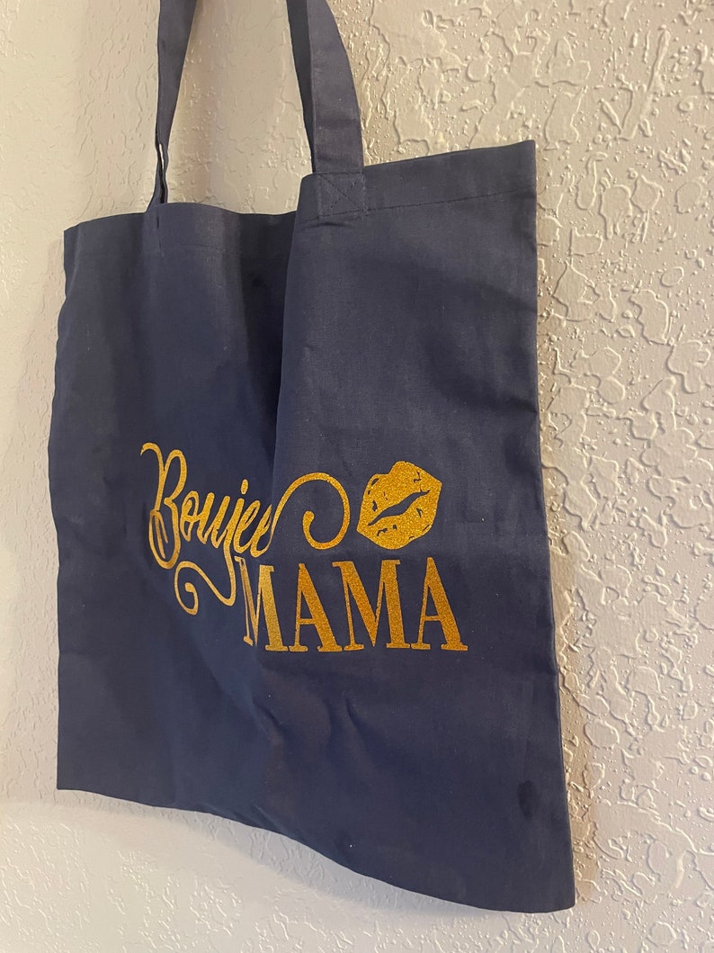 May include: A navy blue tote bag with gold glitter lettering that says "Boujee Mama" and a gold glitter lip print.