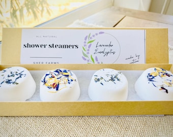 May include: A box of four white shower steamers with lavender and eucalyptus scents. The box is labeled "All Natural Shower Steamers" and "Sher Farms".