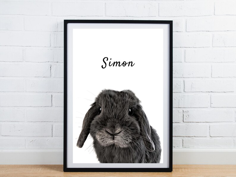 May include: Framed print featuring a close-up of a gray rabbit with floppy ears. The name "Simon" is written in cursive above the rabbit. The print is in a black frame and is displayed against a white brick wall.