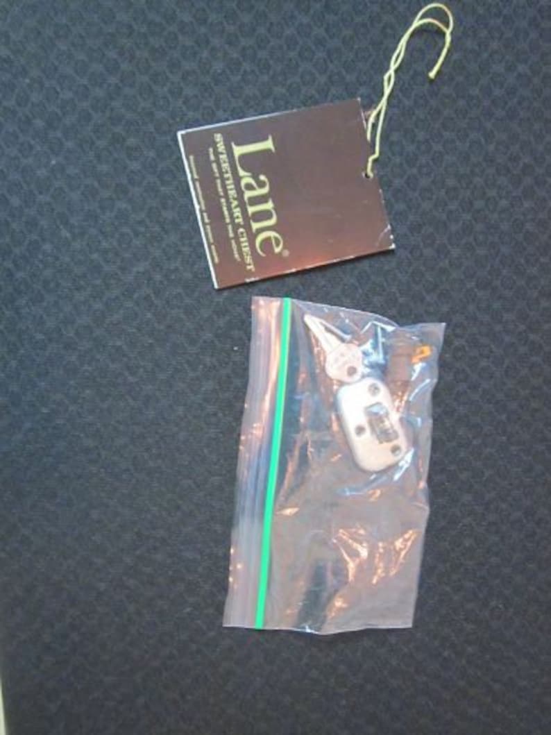 Może przedstawiać: Brązowa papierowa etykieta z tekstem "Lane Sweetheart Chest" i mały srebrny klucz w przezroczystym plastikowym woreczku.