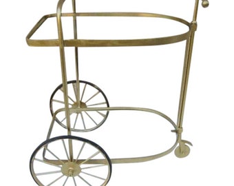 Op de afbeelding: Een gouden metalen serveerwagen met twee verdiepingen en vier wielen. De wagen heeft een handvat aan de zijkant en een ovaalvormige bovenste verdieping.
