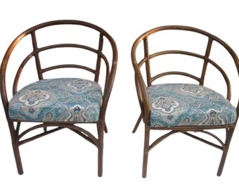 May include: Two brown wicker chairs with a blue and white patterned cushion. The chairs have a rounded back and a curved frame.