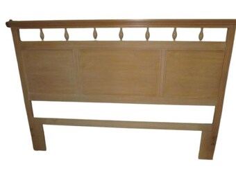 May include: A light wood headboard with a simple design. The headboard has a rectangular shape with a raised panel and a decorative top rail with a series of small, rounded cutouts.