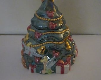 May include: A ceramic Christmas tree cookie jar with a blue and green glaze. The tree is decorated with gold stars, bells, and red and white ornaments. The top of the tree has a gold star and a small, white bird.