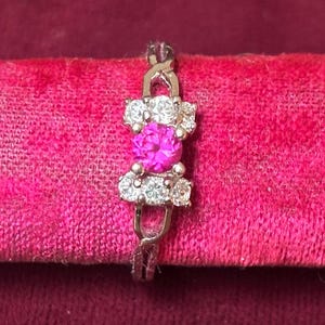 May include: A silver ring with a pink gemstone surrounded by smaller clear gemstones.