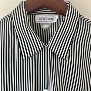 May include: A black and white striped button-down shirt hanging on a wooden hanger. The shirt has vertical stripes and a pointed collar. The label reads "impressions of California". The shirt is buttoned at the top.