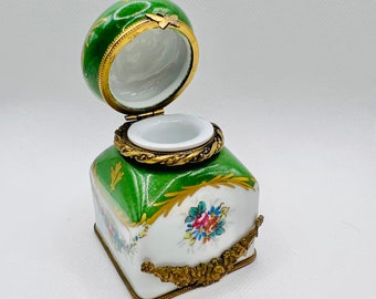 Puede incluir: Un tintero de porcelana verde y blanco con detalles dorados y diseños florales. La tapa está abierta y el tintero está vacío.