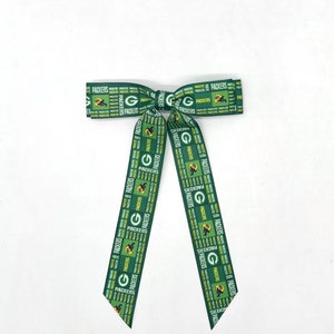 May include: Green and yellow ribbon bow with the words "Packers" repeated throughout. The ribbon is tied in a bow with the ends hanging down.