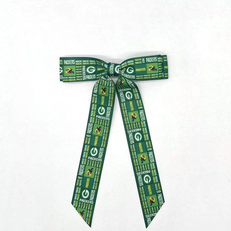 May include: Green and yellow ribbon bow with the words "Packers" repeated throughout. The ribbon is tied in a bow with the ends hanging down.