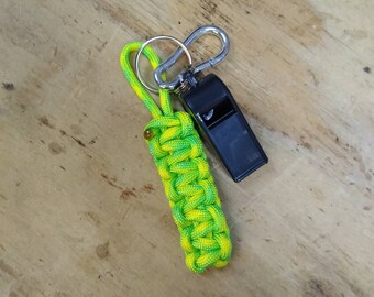 May include: A green and yellow paracord keychain with a black whistle and a silver carabiner.
