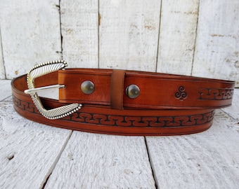 May include: A brown leather belt with a silver buckle and an intricate design. The belt has a Celtic knot design and is made of high-quality leather.