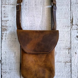 May include: A brown leather crossbody bag with a flap closure. The bag has a distressed look and is made of a thick, durable leather.