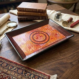 May include: A rectangular decorative tray featuring a central circular medallion with deer illustrations, surrounded by intricate orange, red, and gold floral patterns. The tray has a dark brown border and a glossy finish, showcasing detailed artwork.