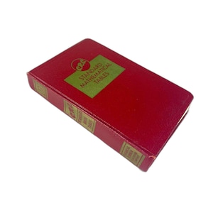 Peut inclure: Un livre rouge rectangulaire avec le titre "Standard Mathematical Tables" en lettres vertes. Le livre a une couverture texturée et des lettres dorées sur le dos. Le livre est légèrement incliné.