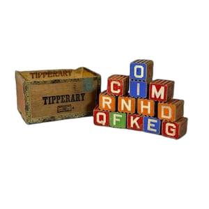 May include: Wooden alphabet blocks with colorful letters and numbers, stacked in a pyramid shape. The blocks are in a wooden box with the word "Tipperary" printed on it. The box is brown with green and gold accents.
