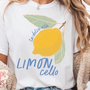 K&ouml;nnte beinhalten: Wei&szlig;es T-Shirt mit einer gelben Zitronenillustration, gr&uuml;nen Bl&auml;ttern und dem Text "La dolce vita" und "Limoncello" in Blau. Ein l&auml;ssiges Kleidungsst&uuml;ck.