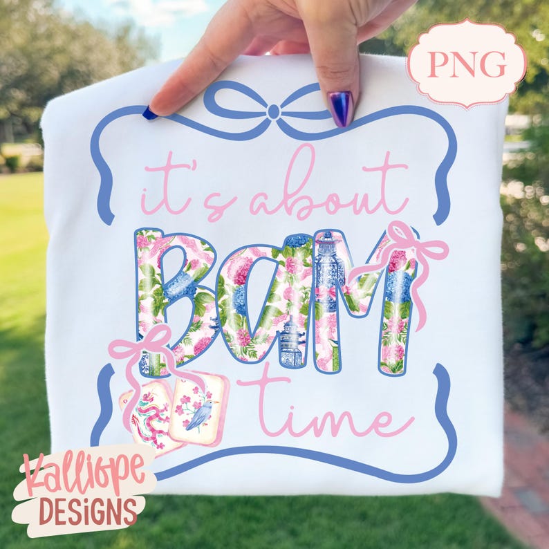May include: White t-shirt with a blue and pink floral design that spells out "BAM" in large letters. The text "it's about time" is written in pink script. The design includes a blue border and pink bows.