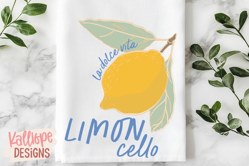 K&ouml;nnte beinhalten: Wei&szlig;es K&uuml;chentuch mit einer gelben Zitronenillustration und den Worten "La dolce vita" und "Limoncello" in Blau. Die Zitrone hat gr&uuml;ne Bl&auml;tter und einen braunen Stiel. Das Tuch liegt auf einer Marmoroberfl&auml;che.
