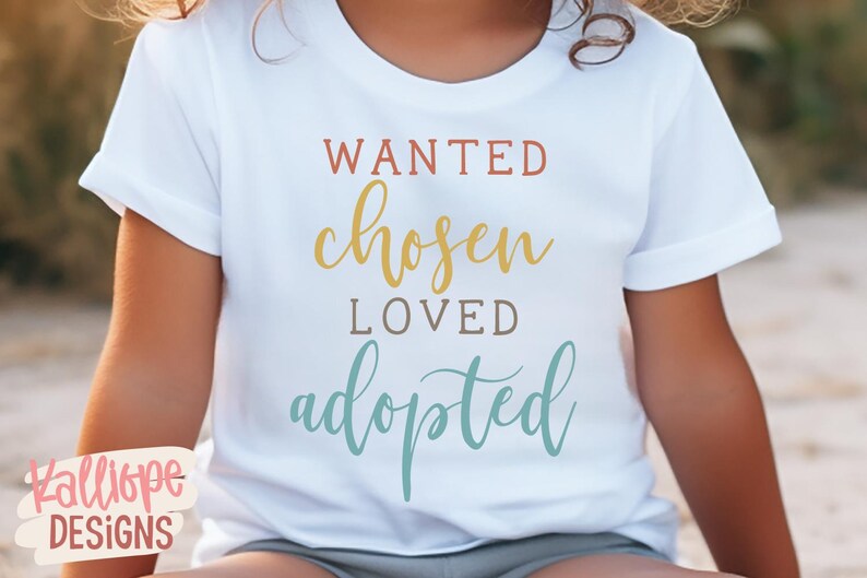 May include: White t-shirt with the words "WANTED, chosen, LOVED, adopted" in various colours. The text is in a handwritten style font. The shirt is short-sleeved.