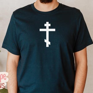 Op de afbeelding: Marineblauw T-shirt met een wit orthodox kruisontwerp. Het kruis heeft drie horizontale balken en een schuine voetbalk. Het shirt is gemaakt van een zacht materiaal.