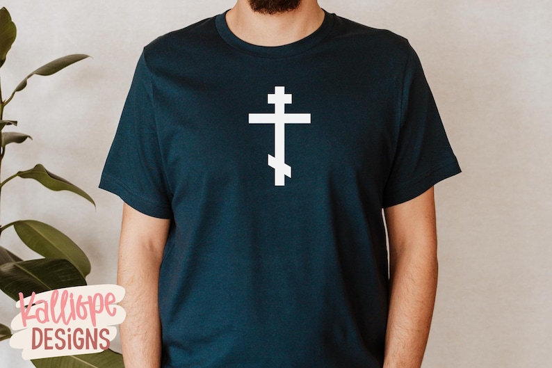 Op de afbeelding: Marineblauw T-shirt met een wit orthodox kruisontwerp. Het kruis heeft drie horizontale balken en een schuine voetbalk. Het shirt is gemaakt van een zacht materiaal.