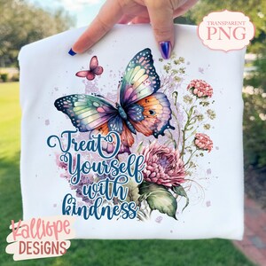 May include: White t-shirt featuring a watercolor butterfly with colorful wings and the text "Treat Yourself with Kindness." The design includes pink flowers and a smaller butterfly. The brand name "Kalliope Designs" is also visible.