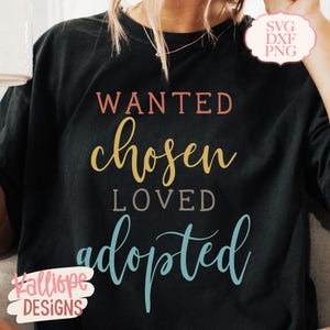 May include: Black t-shirt with the words "WANTED, chosen, LOVED, adopted" in various colours. The shirt also has the text "SVG DXF PNG" in a pink circle and the text "Kalliope DESIGNS" in a pink oval.