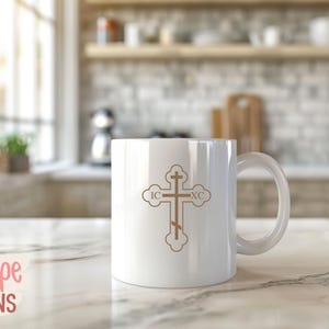 Op de afbeelding: Witte keramische mok met een goudkleurig orthodox kruisontwerp. Het kruis, met de letters IC en XC, staat in het midden van de mok. De mok heeft een grote handgreep en staat op een marmeren aanrecht. De mok is ongeveer 10 cm hoog.