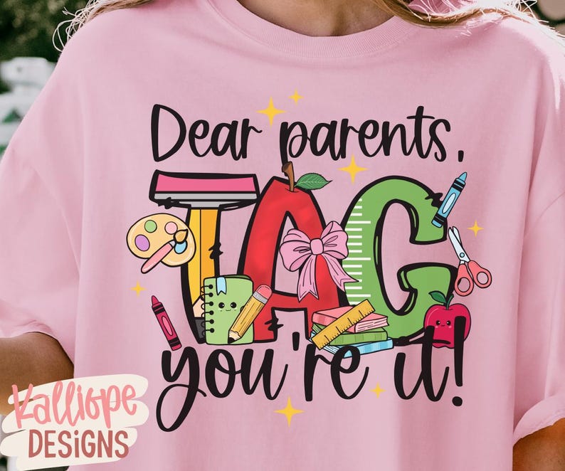 May include: Pink t-shirt with the text "Dear parents, TAG you're it!" in black script. The design includes a red apple, green ruler, and school supplies. The shirt has a crew neck and short sleeves.