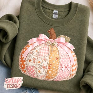 May include: An olive green crewneck sweatshirt featuring a large, central pumpkin applique made of various fabric patches in orange, pink, and white with floral, polka dot, and gingham patterns, accented by a pink satin bow and a small rose.