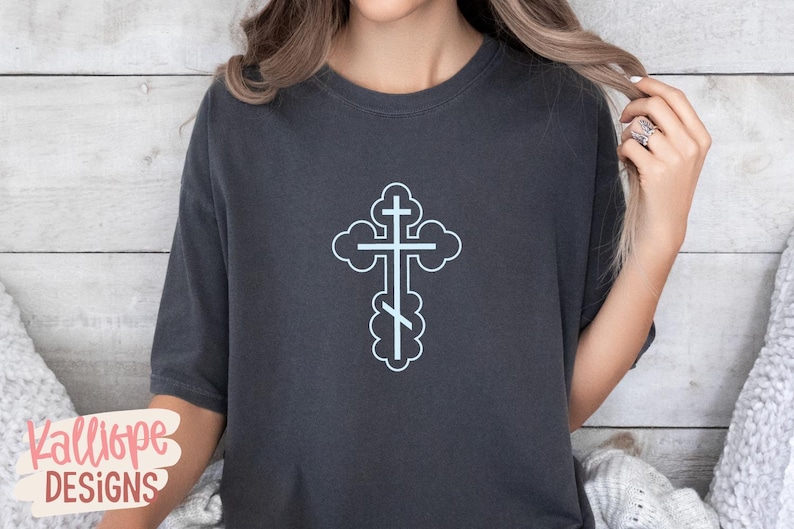 Op de afbeelding: Donkergrijs T-shirt met een lichtblauw orthodox kruisontwerp. Het kruis is omlijnd met een wolkvorm. Het shirt heeft korte mouwen en een ronde hals. De merknaam "Kalliope DESIGNS" is linksonder zichtbaar.
