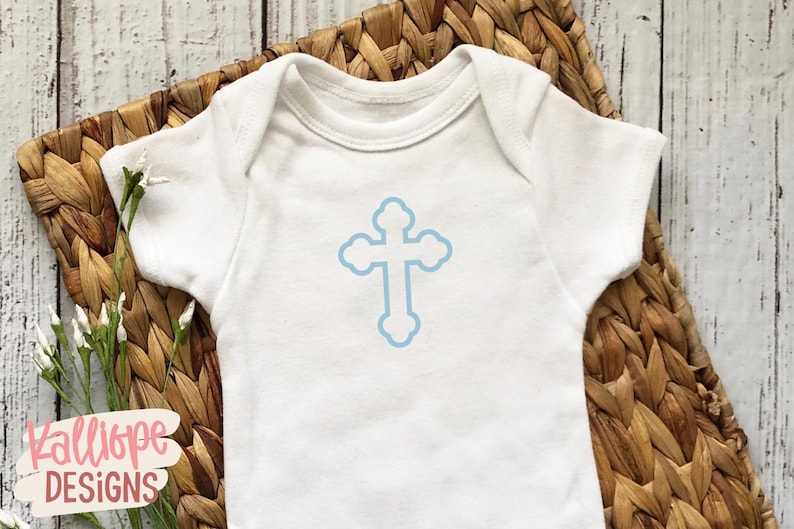 Op de afbeelding: Witte babybody met een lichtblauw kruisontwerp. De body ligt op een gevlochten mand. De tekst "Kalliope Designs" is linksonder zichtbaar. Er zijn ook een paar takjes witte bloemen.
