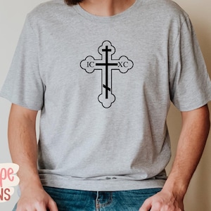 Op de afbeelding: Een lichtgrijs t-shirt met een zwart orthodox kruisontwerp. Het kruis heeft de letters IC en XC. Het t-shirt is gemaakt van een zacht materiaal en is geschikt voor dagelijks gebruik.