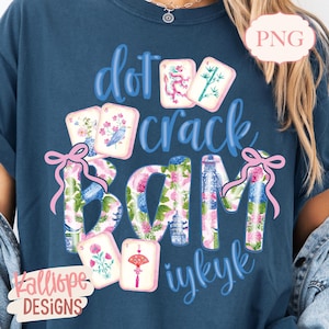 May include: Navy blue t-shirt with a colorful graphic design. The design features the words "dot crack bam" in a floral pattern, surrounded by playing cards. The text "iykyk" is also included. The shirt has the text "Calliope Designs" on the bottom left.