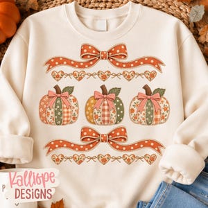 May include: A cream-coloured crewneck sweatshirt featuring a graphic print of three pumpkins with patchwork patterns, each adorned with a pink bow. The design includes two orange polka-dot ribbons and rows of small hearts with floral motifs.