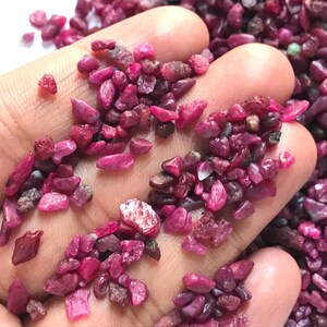 Op de afbeelding: Een verzameling kleine, ruwe robijn-edelsteensplinters in dieproze en magentakleuren. Deze natuurlijke, ongepolijste stenen hebben onregelmatige, grillige vormen en vari&euml;rende gradaties van doorschijnendheid, met een levendig en verzadigd kleurenpalet.