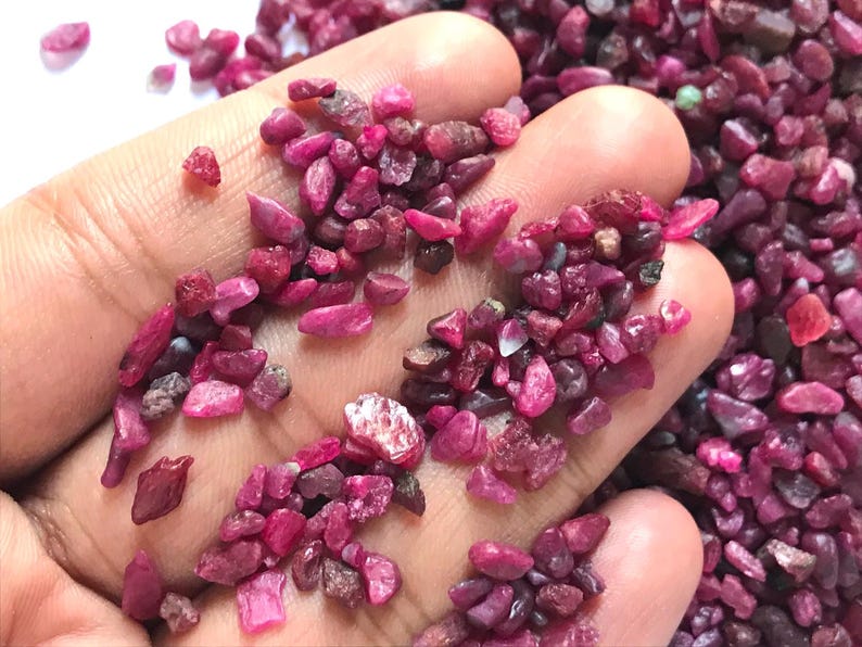Op de afbeelding: Een verzameling kleine, ruwe robijn-edelsteensplinters in dieproze en magentakleuren. Deze natuurlijke, ongepolijste stenen hebben onregelmatige, grillige vormen en vari&euml;rende gradaties van doorschijnendheid, met een levendig en verzadigd kleurenpalet.