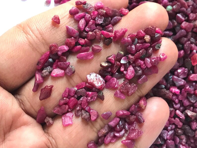 Op de afbeelding: Een verzameling kleine, ruwe, ongepolijste robijn-edelstenen in verschillende tinten diep roze en magenta. Deze natuurlijke mineraalfragmenten hebben onregelmatige, grillige vormen en een matte tot licht doorschijnende textuur in hun ruwe staat.