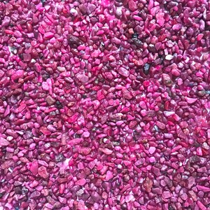 Op de afbeelding: Een verzameling kleine, onregelmatig gevormde steentjes in levendige tinten magenta en dieproze. De stenen hebben een glanzende, reflecterende textuur met vari&euml;rende groottes en grillige randen, wat zorgt voor een dichte, uniforme laag mineralen.