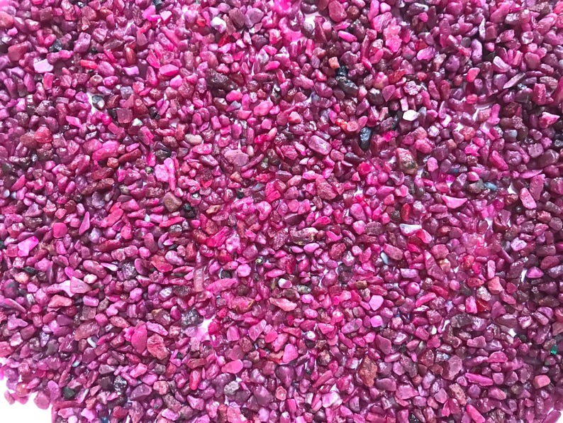 Op de afbeelding: Een verzameling kleine, onregelmatig gevormde steentjes in levendige tinten magenta en dieproze. De stenen hebben een glanzende, reflecterende textuur met vari&euml;rende groottes en grillige randen, wat zorgt voor een dichte, uniforme laag mineralen.