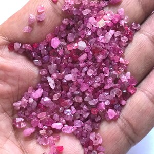 Op de afbeelding: Een verzameling kleine, ruwe, ongepolijste edelsteenfragmenten in verschillende tinten roze, magenta en dieprood. Deze kleine, onregelmatige minerale stukjes hebben een doorschijnend tot ondoorzichtig uiterlijk met een natuurlijke textuur.