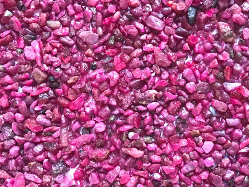 Op de afbeelding: Een verzameling kleine, onregelmatige, getrommelde edelsteenfragmenten in levendige tinten magenta en dieproze. De stenen hebben een gepolijste, glanzende textuur met vari&euml;rende niveaus van doorschijnendheid en af en toe donkere insluitingen.