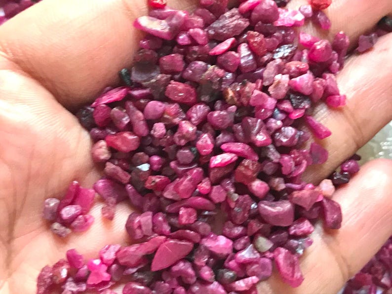 Op de afbeelding: Een verzameling kleine, ruwe, ongepolijste robijn-edelstenen in verschillende tinten diep roze en levendig rood. Deze losse, onregelmatige mineraalfragmenten hebben een getextureerd, mat oppervlak en zijn in een losse hoop gerangschikt.