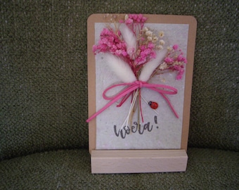 Wooden stand with a handmade paper card and a bunch of dried flowers